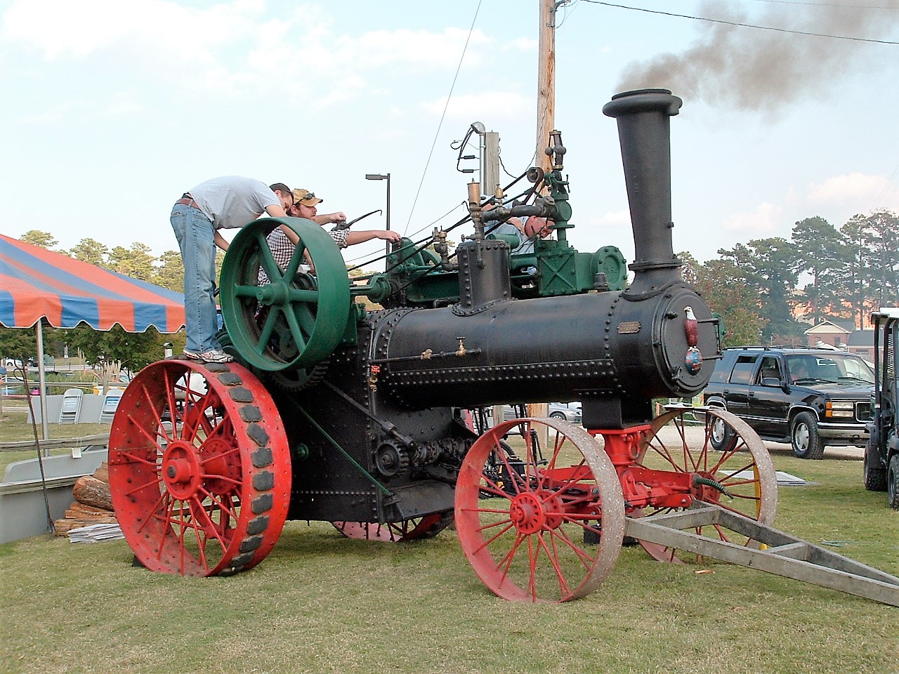 The Old Nancy steam traction engine, with red wheels and a green flywheel, and two men working on it